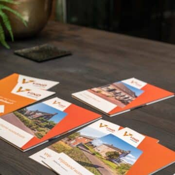 Oranje makelaarsbrochures van VIND uitgespreid op een donkere houten tafel.