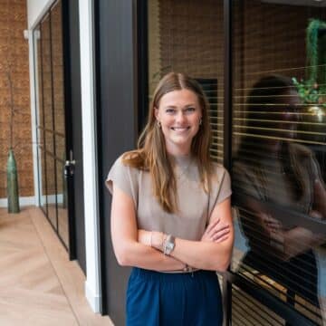 Glimlachende adviseur met gekruiste armen in modern kantoor met houten wandpanelen en groen.