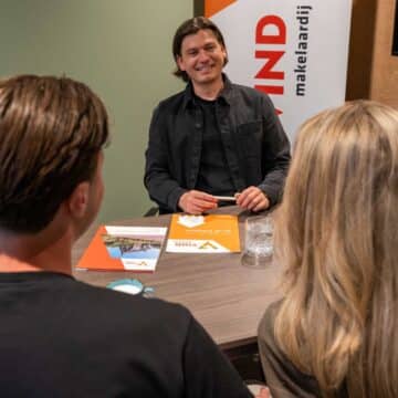 Een makelaar bespreekt met een stel aan tafel de verkoop van hun woning bij VIND Makelaardij.