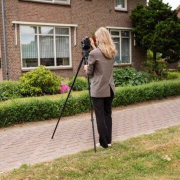 Vrouwelijke medewerker fotografeert met een camera op statief de gevel van een bakstenen woonhuis.