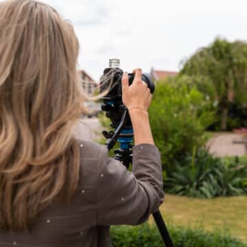 Vrouwelijke medewerker fotografeert met camera op statief een woonwijk op een bewolkte dag.