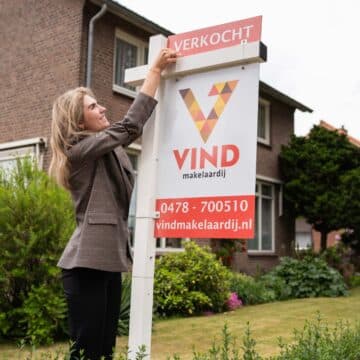 Makelaar plaatst een Verkocht-bordje op een makelaarsbord van VIND Makelaardij voor een woonhuis.