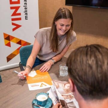 Adviseur bespreekt lachend een brochure van VIND Makelaars met klanten aan een vergadertafel.