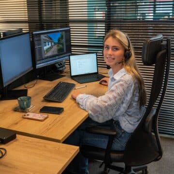 Een adviseur met headset zit achter een bureau met meerdere beeldschermen op kantoor.